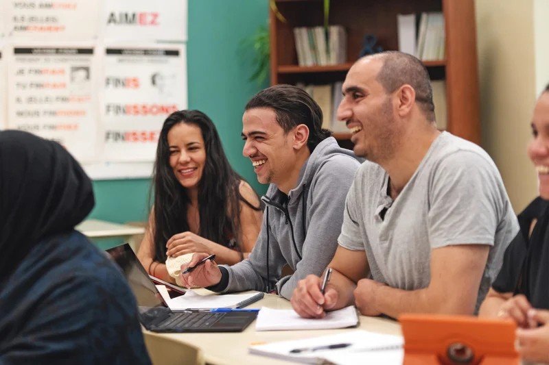 Adult ESL students smiling and taking notes together in a classroom
