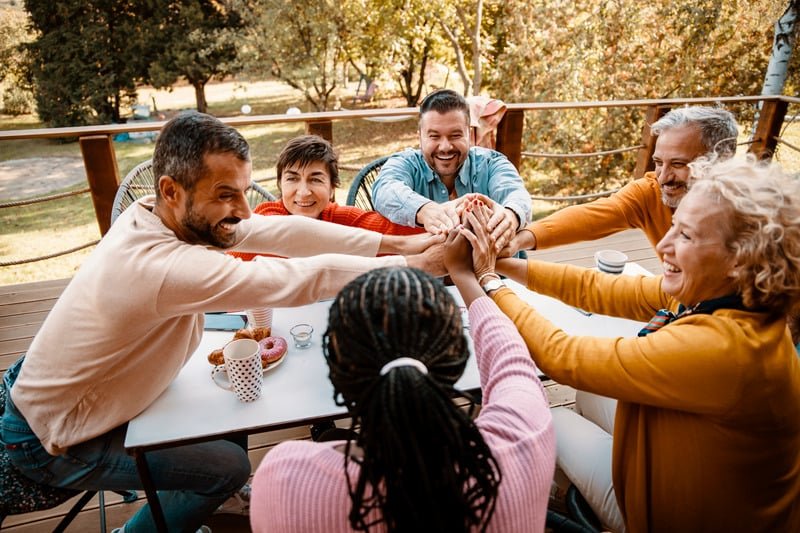 A diverse group of friends joining hands around a table outdoors