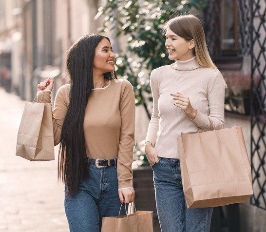 Two friends walking outside with shopping bags, chatting and smiling