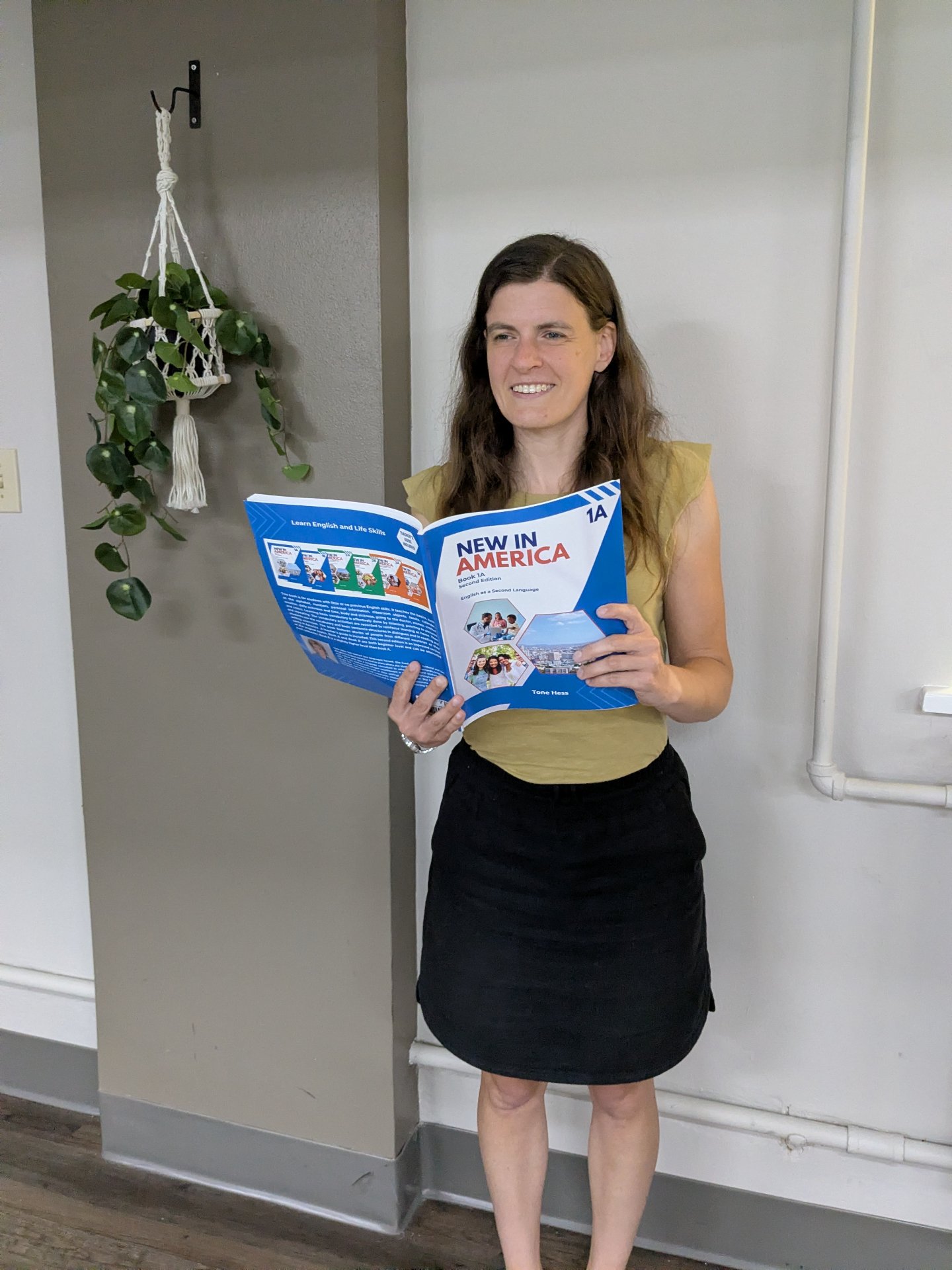 A teacher smiling while holding open a New in America Book 1A workbook