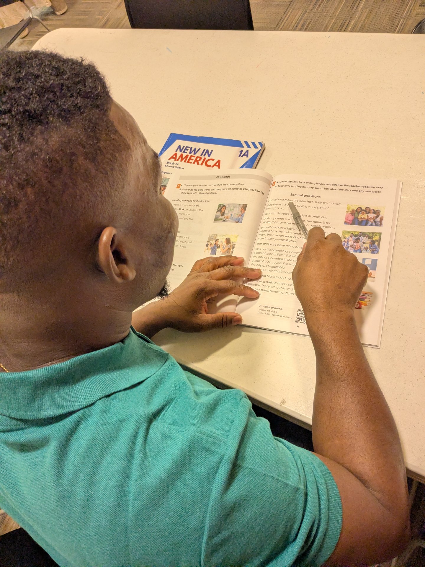 A student reading the Samuel and Marie story spread in a New in America Book 1A workbook