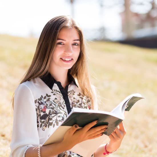 A young woman smiling while reading an ESL workbook outdoors